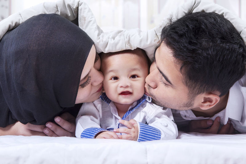 Muslim mother and father kissing child, just like Prophet Muhammad
